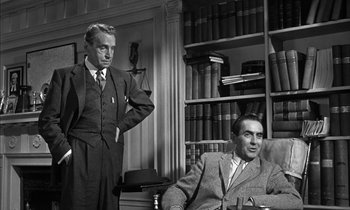 Movie still from “Witness for the Prosecution” (1957), directed by Billy Wilder – A man standing next to a man sitting in a chair in a room; Medium shot, Low angle