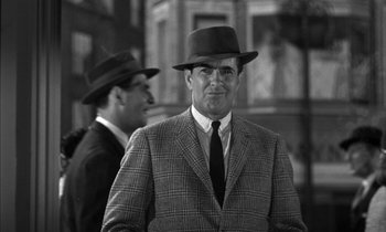 Movie still from “Witness for the Prosecution” (1957), directed by Billy Wilder – A man in a suit and hat standing next to another man in a suit; Medium shot, Over the shoulder angle