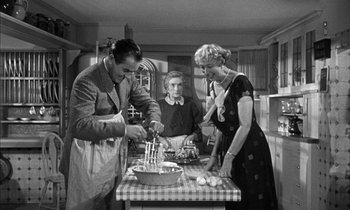 Movie still from “Witness for the Prosecution” (1957), directed by Billy Wilder – A man and two women in a kitchen preparing a meal; Medium shot, High angle