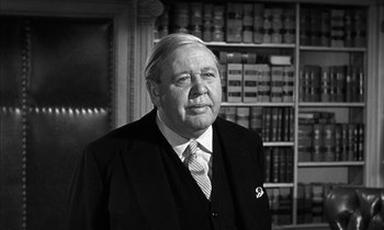 Movie still from “Witness for the Prosecution” (1957), directed by Billy Wilder – An older man wearing a suit and tie in front of a book case; Close Up shot, Low angle