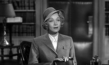 Movie still from “Witness for the Prosecution” (1957), directed by Billy Wilder – An old photo of a woman wearing a hat and a suit; Medium shot, Low angle