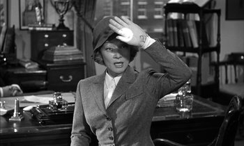 Movie still from “Witness for the Prosecution” (1957), directed by Billy Wilder – A woman wearing a suit and hat in an office setting; Medium shot, Over the shoulder angle