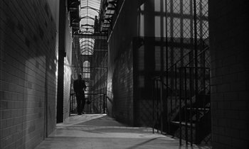 Movie still from “Witness for the Prosecution” (1957), directed by Billy Wilder – A person standing in a hallway with a metal fence; Wide shot, Low angle