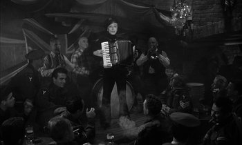 Movie still from “Witness for the Prosecution” (1957), directed by Billy Wilder – A man playing an accordion in front of a group of people; Wide shot, Low angle
