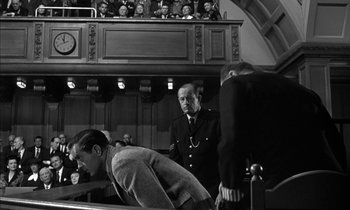 Movie still from “Witness for the Prosecution” (1957), directed by Billy Wilder – Two men in suits and ties in front of a group of people; Medium shot, Over the shoulder angle