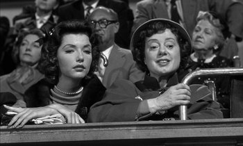 Movie still from “Witness for the Prosecution” (1957), directed by Billy Wilder – Two women sitting next to each other in a crowd; Medium shot, Over the shoulder angle