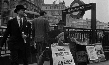 Movie still from “Witness for the Prosecution” (1957), directed by Billy Wilder – An old black - and - white photo of a man standing in front of an underground sign; Wide shot, High angle