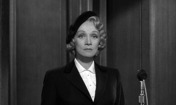 Movie still from “Witness for the Prosecution” (1957), directed by Billy Wilder – An older woman wearing a black suit and a black hat; Medium shot, Low angle