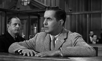 Movie still from “Witness for the Prosecution” (1957), directed by Billy Wilder – A man sitting at a table in front of a window; Medium shot, Low angle