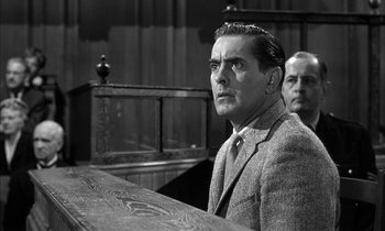 Movie still from “Witness for the Prosecution” (1957), directed by Billy Wilder – A man sitting in front of a wooden table; Medium shot, Low angle