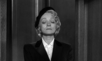 Movie still from “Witness for the Prosecution” (1957), directed by Billy Wilder – An older woman wearing a black suit and a black hat; Close Up shot, Low angle