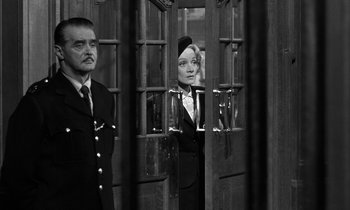 Movie still from “Witness for the Prosecution” (1957), directed by Billy Wilder – A man and a woman standing next to each other in front of a door; Medium shot, Low angle
