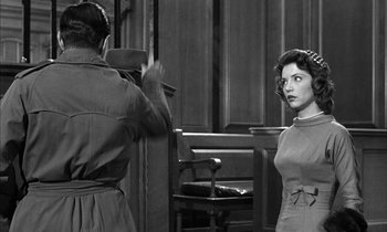 Movie still from “Witness for the Prosecution” (1957), directed by Billy Wilder – A woman standing in front of a man in a court room; Medium shot, Over the shoulder angle