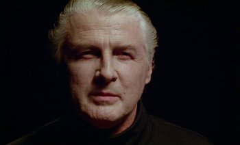 Movie still from “Wittgenstein” (1993), directed by Derek Jarman – An older man with white hair and a black shirt; Close Up shot, Low angle