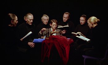 Movie still from “Wittgenstein” (1993), directed by Derek Jarman – A group of people sitting around a table reading books; Medium shot, High angle