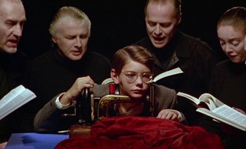 Movie still from “Wittgenstein” (1993), directed by Derek Jarman – A young boy sitting in front of an old sewing machine; Medium shot, High angle