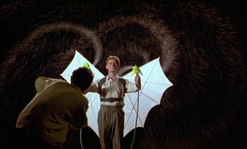 Movie still from “Wittgenstein” (1993), directed by Derek Jarman – A man holding an umbrella while standing in the rain; Wide shot, Low angle