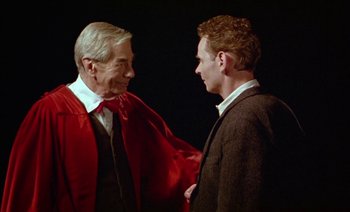 Movie still from “Wittgenstein” (1993), directed by Derek Jarman – Two men are shaking hands while wearing robes; Medium shot, Over the shoulder angle