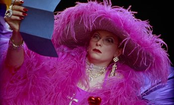 Movie still from “Wittgenstein” (1993), directed by Derek Jarman – A woman wearing a pink hat and a pink feather boa; Close Up shot, Over the shoulder angle