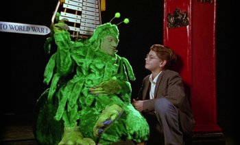 Movie still from “Wittgenstein” (1993), directed by Derek Jarman – A man sitting next to a green creature; Medium shot, Low angle