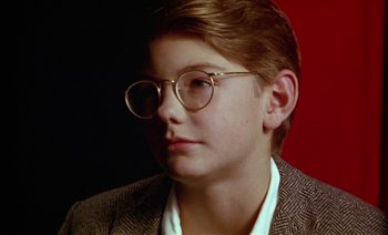 Movie still from “Wittgenstein” (1993), directed by Derek Jarman – A young man wearing glasses and a jacket; Close Up shot, High angle