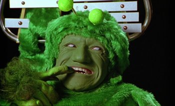 Movie still from “Wittgenstein” (1993), directed by Derek Jarman – A person dressed as a green creature with tennis balls on their head; Extreme Close Up shot, High angle