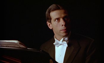 Movie still from “Wittgenstein” (1993), directed by Derek Jarman – A person wearing a suit and bow tie; Close Up shot, Low angle