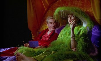 Movie still from “Wittgenstein” (1993), directed by Derek Jarman – A man and a woman sitting on a couch smoking a cigarette; Medium shot, High angle