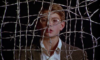Movie still from “Wittgenstein” (1993), directed by Derek Jarman – A man with glasses behind barbed wire; Close Up shot, Low angle