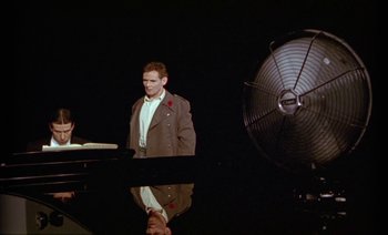 Movie still from “Wittgenstein” (1993), directed by Derek Jarman – A man standing in front of an electric fan; Wide shot, High angle
