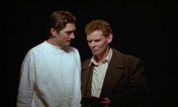 Movie still from “Wittgenstein” (1993), directed by Derek Jarman – Two men looking at each other while holding a cell phone; Medium shot, Low angle