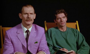 Movie still from “Wittgenstein” (1993), directed by Derek Jarman – Two men sitting next to each other on a chair; Medium shot, Over the shoulder angle