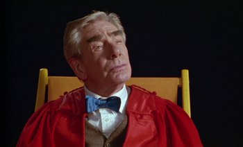 Movie still from “Wittgenstein” (1993), directed by Derek Jarman – An older man sitting in a chair wearing a red robe; Close Up shot, Low angle