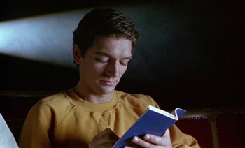 Movie still from “Wittgenstein” (1993), directed by Derek Jarman – A young man reading a book in a dark room; Close Up shot, High angle