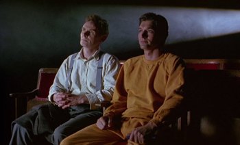 Movie still from “Wittgenstein” (1993), directed by Derek Jarman – Two men sitting on a bench looking at something; Medium shot, Low angle