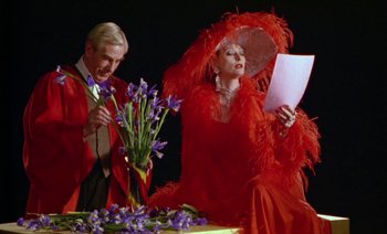 Movie still from “Wittgenstein” (1993), directed by Derek Jarman – A man and a woman dressed in red sitting next to a table; Medium shot, Low angle
