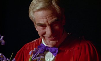 Movie still from “Wittgenstein” (1993), directed by Derek Jarman – An older man wearing a red robe and a purple bow tie; Close Up shot, Low angle