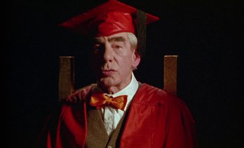 Movie still from “Wittgenstein” (1993), directed by Derek Jarman – An older man wearing a red graduation cap and gown; Close Up shot, High angle