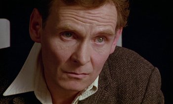 Movie still from “Wittgenstein” (1993), directed by Derek Jarman – A man's face in a brown jacket; Close Up shot, High angle