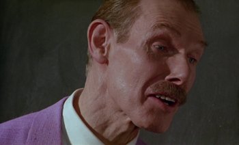 Movie still from “Wittgenstein” (1993), directed by Derek Jarman – An older man in a purple jacket looks at the camera; Close Up shot, Low angle