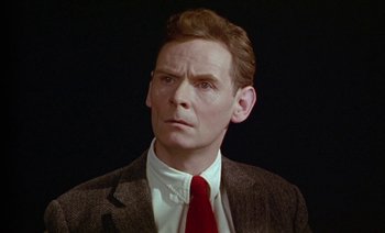 Movie still from “Wittgenstein” (1993), directed by Derek Jarman – A person wearing a suit and tie; Close Up shot, High angle