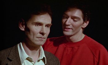 Movie still from “Wittgenstein” (1993), directed by Derek Jarman – A man standing next to another man in front of a wall; Close Up shot, Over the shoulder angle