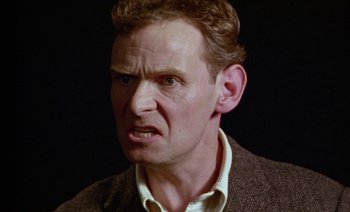 Movie still from “Wittgenstein” (1993), directed by Derek Jarman – A person wearing a suit and tie; Close Up shot, Low angle