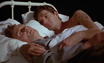 Movie still from “Wittgenstein” (1993), directed by Derek Jarman – Two men laying in a hospital bed together; Medium shot, High angle