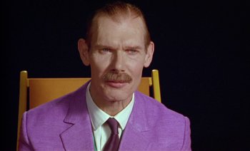 Movie still from “Wittgenstein” (1993), directed by Derek Jarman – A man in a purple suit and a purple tie; Close Up shot, Low angle