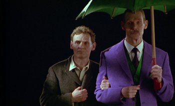 Movie still from “Wittgenstein” (1993), directed by Derek Jarman – A man in a suit holding an umbrella next to another man in a suit holding an umbrella; Medium shot, Low angle