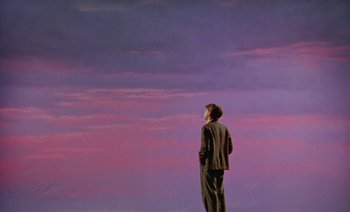 Movie still from “Wittgenstein” (1993), directed by Derek Jarman – A man standing in front of a purple sky; Wide shot, Low angle