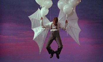 Movie still from “Wittgenstein” (1993), directed by Derek Jarman – A man holding a bunch of white umbrellas in the air; Wide shot, Overhead angle