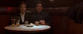 Movie still from “Wonder Boys” (2000), directed by Curtis Hanson – A man sitting at a table smoking a cigarette and holding a drink; Medium shot, Low angle