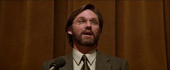 Movie still from “Wonder Boys” (2000), directed by Curtis Hanson – A man in a suit and glasses is speaking at a podium; Close Up shot, Low angle